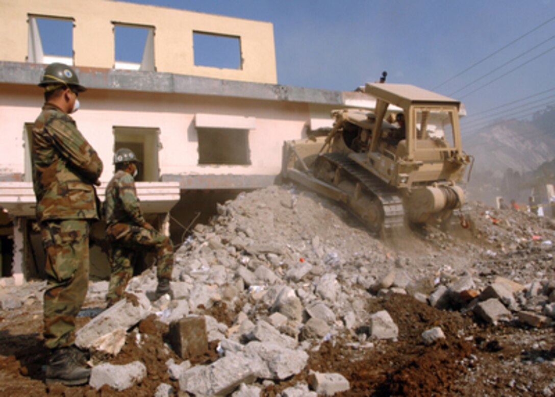 Two U.S. Navy Seabees watch a bulldozer operator clear debris at the Ministry of Education Building in Muzaffarabad, Pakistan, on Dec. 1, 2005. The Seabees are attached to Naval Mobile Construction Battalion 74, deployed from Gulfport, Miss. The Department of Defense is supporting the State Department by providing disaster relief supplies and services following the massive earthquake that struck Pakistan and parts of India and Afghanistan. 