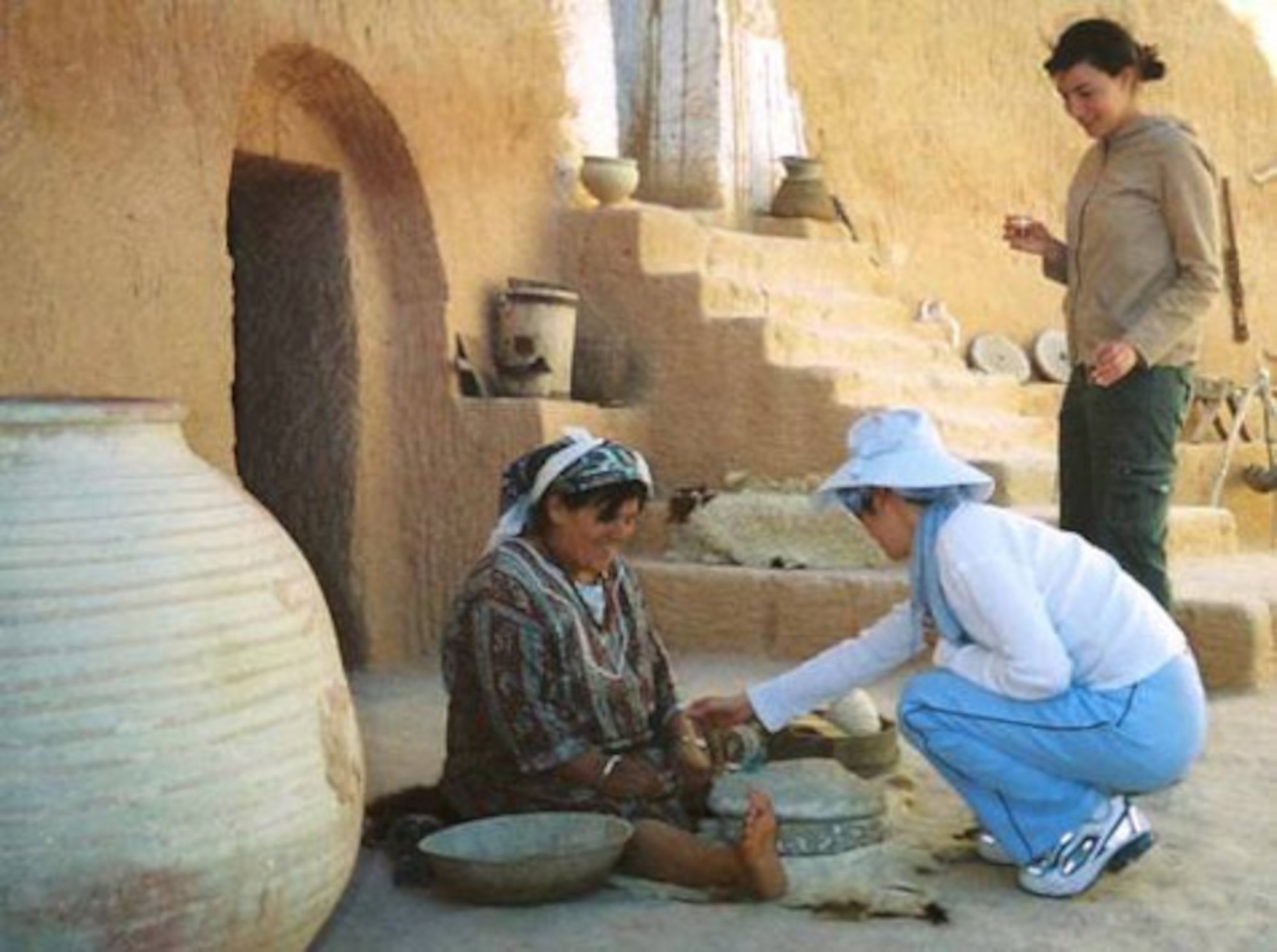 TATAOUINE, Tunisia (AFMCNS) -- First lieutenant Dan Liu helps a Tunisian woman make flour out of grains in her Berber home on the outskirts of the Sahara Desert as Capt. Laurie Wax watches them during their recent four-week Language and Area Studies Immersion trip. The LASI is designed to build a force of culturally savvy officers who can meet the need of communicating with a developing world. Lieutenant Liu is from Sembach Air Base, Germany and Captain Wax is from Monterey, Calif. (Air Force photo by 1st Lt. Kristen Duncan)