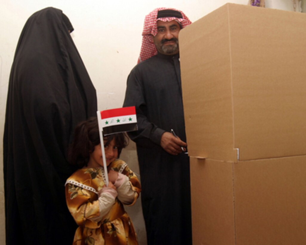 A little girl clutches an Iraqi flag as her parents vote in a polling booth at the Al-Kunaytarah School in Jurf as Sakhr District, Iraq, on Dec. 15, 2005. Iraqi citizens are voting to elect Iraq's first free, permanent parliamentary government. 