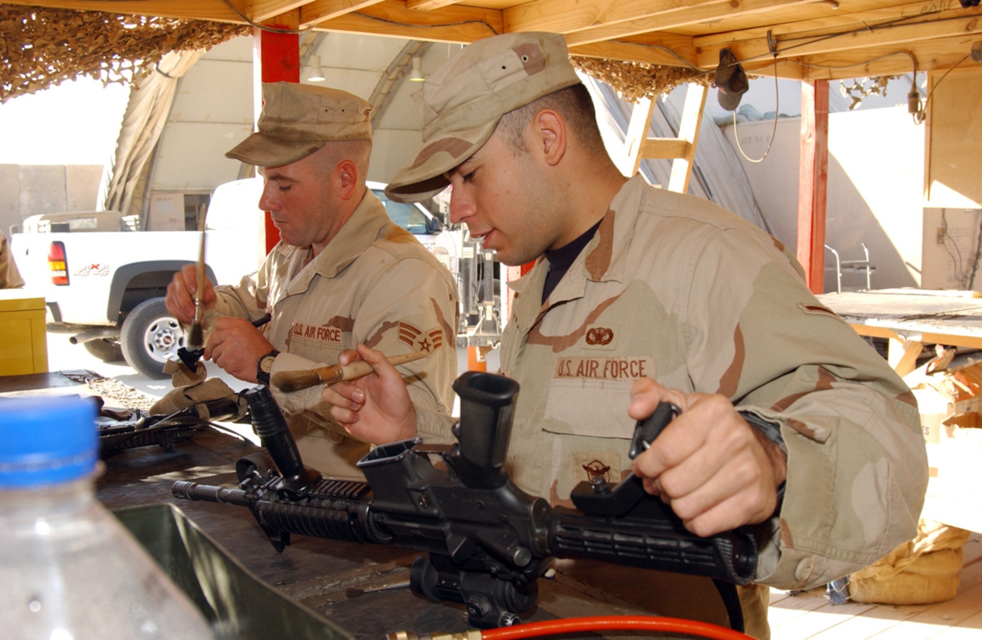 BALAD AIR BASE, Iraq (AFPN) -- Airman Dwayne Solis (right) and Senior Airman Derrick Meadors clean their weapons. The Airmen are with the 732nd Expeditionary Logistics Readiness Squadron. The squadron helps provide security escorts for convoy missions leaving the base. (U.S. Air Force photo by Staff Sgt. Tammie Moore)