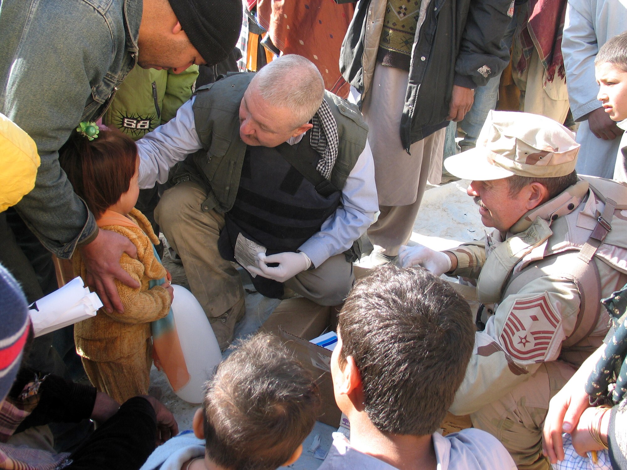 KABUL, Afghanistan (AFPN) -- Jim Norman (center) and Senior Master Sgt. Jim Thomson provide first aid to an Afghan girl at Bagrami Village refugee camp here.  People from nearby Camp Eggers visited the camp to provide toys, snacks, clothing and other supplies.  Mr. Norman is from Henderson, Nevada, and Sergeant Thomson is deployed from March Air Reserve Base, Calif.  (U.S. Air Force photo by Capt. Dave Huxsoll) 