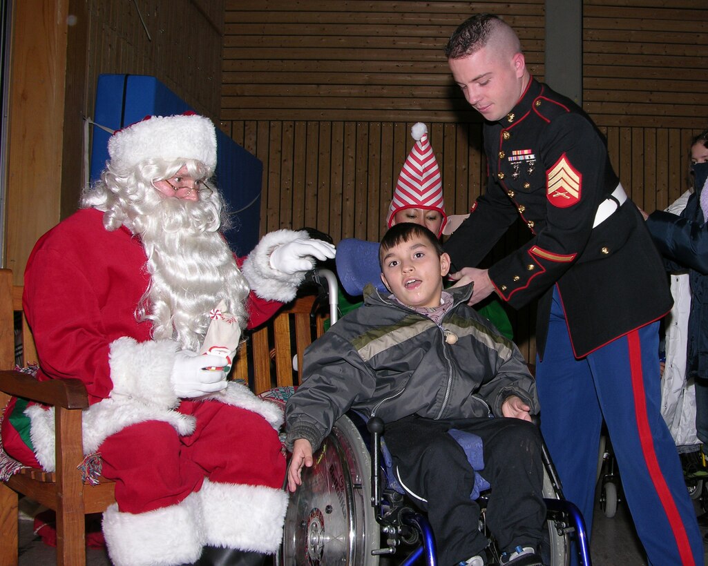 STUTTGART, Germany (Dec. 20, 2005) Sgt. Robert Hatchley, a guard force Marine with U.S. Marine Corps Forces Europe, assists a wheelchair-bound student so he can get his photo taken with Santa during a school Christmas celebration.  Santa along with Marines from MARFOREUR attended the celebration, bringing Christmas stockings and taking pictures of the students with Santa at the Schule für Körperbehindertemade, a handicapped children's school in Stuttgart, Germany.