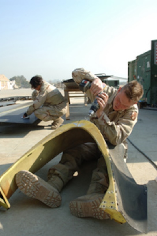 Spc. Michael Johnson, U.S. Army, uses his legs as an impromptu workbench as he drills on a replacement aircraft part on Qasim Air Base, Pakistan, on Dec. 18, 2005. Johnson is assigned to Bravo Company of the 7/158th Aviation Regiment, which is part of a multinational task force supporting earthquake relief efforts in Pakistan. 