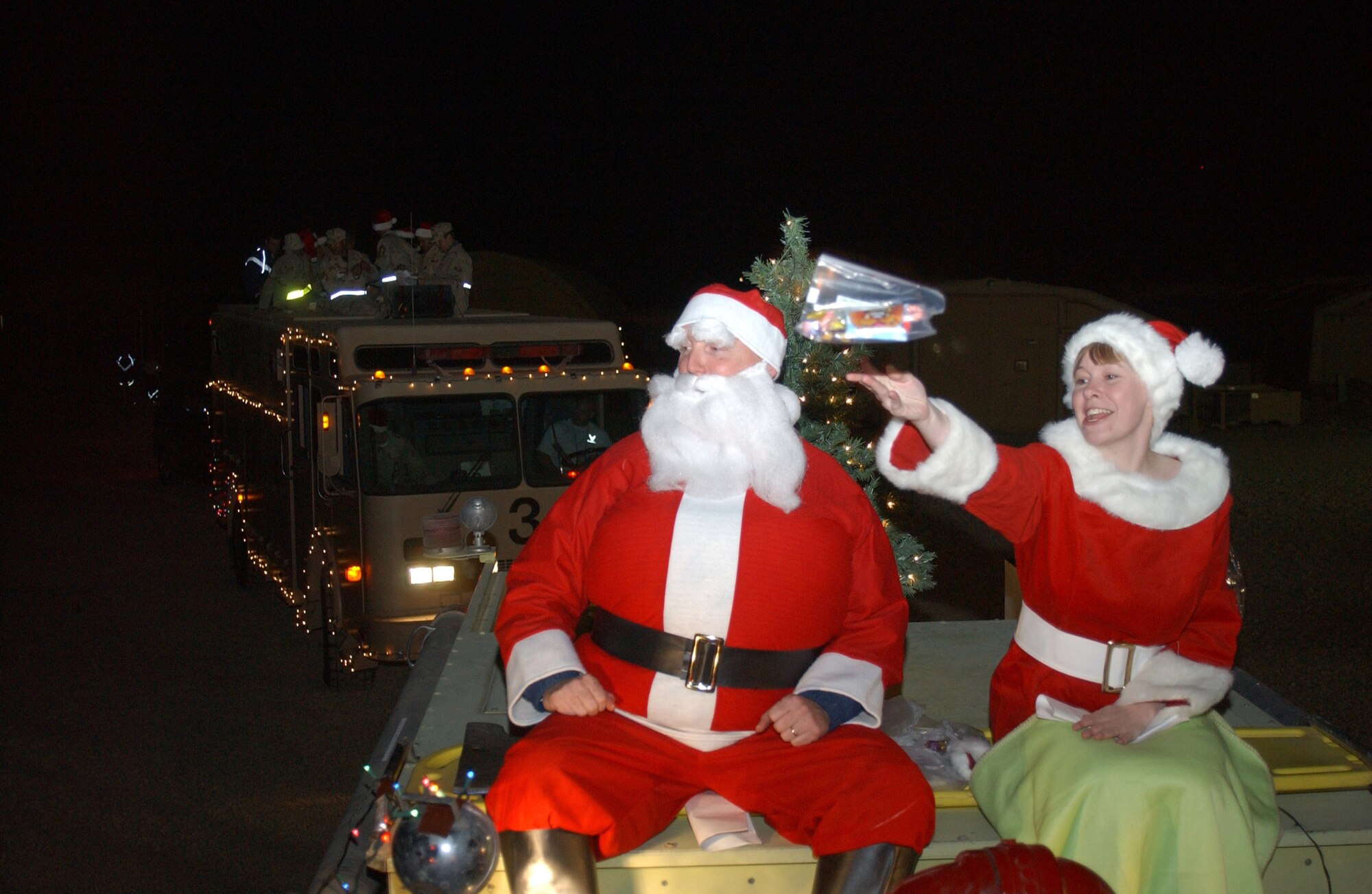 ALI BASE, Iraq (AFPN) -- Mrs. Claus (Staff Sgt. Melissa Farrell) tosses a bag of candy to an Airman who promised Santa (Lt. Col. Richard Houghton), he was good this year.  Santa, Mrs. Claus and the Care Bear singers (carolers in truck behind Santa's sleigh) toured the base spreading cheer, Ho Ho Ho's and some sweet treats Christmas Eve to all servicemembers deployed here.  Sergeant Farrell is in the 407th Expeditionary Services Squadron and Col. Houghton is in the 407th Expeditionary Civil Engineer Squadron.  (U.S. Air Force photo by Tech. Sgt. Paul Dean) 