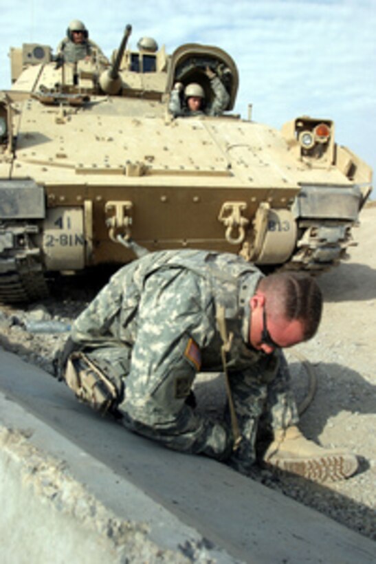 A soldier from the U.S. Army's 4th Infantry Division hooks up a concrete barrier to his Bradley Fighting Vehicle to drag it into position at a checkpoint in Diyarah, Iraq, on Dec. 20, 2005. 