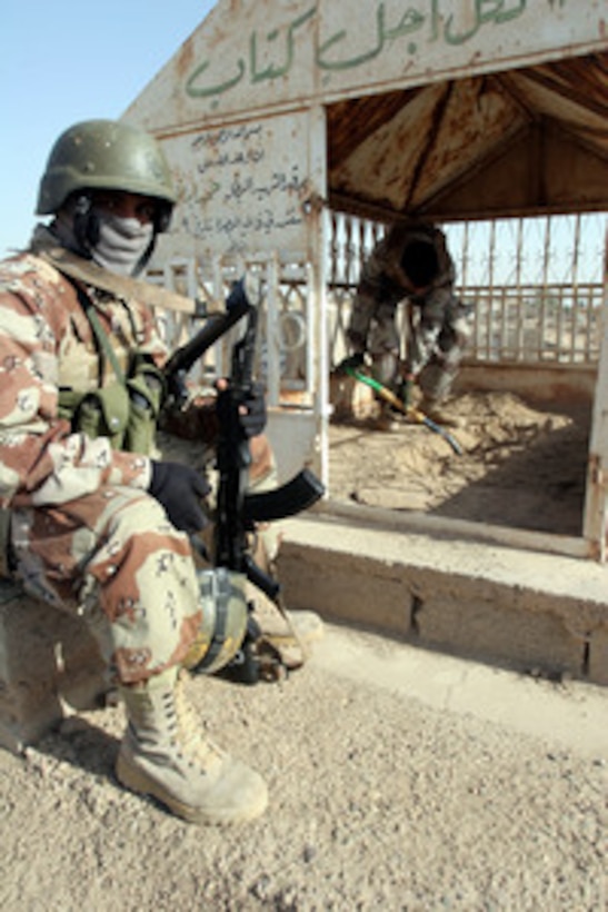 One Iraqi soldier stands watch as another digs for buried weapons during a search of the Jolan Cemetery in Fallujah, Iraq, on Dec. 24, 2005. Soldiers from the 1st Iraqi Infantry Division, 2nd Brigade, 2nd Battalion broadened the search after finding weapons hidden on the grounds. 