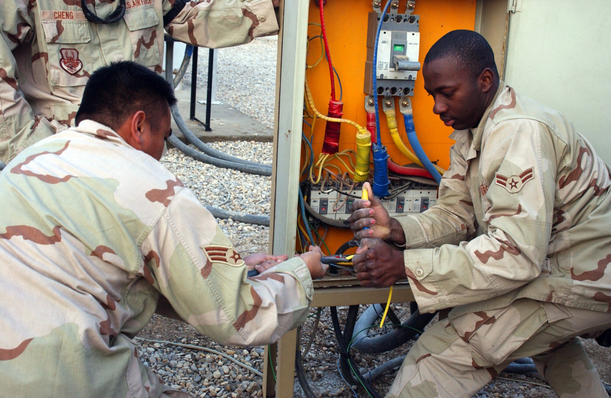 ALI BASE, Iraq (AFPN) -- Heavy rains on Christmas Day seeped into and shorted out wiring that served half of the 407th Air Expeditionary Group headquarters building. Airmen from the 407th Expeditionary Civil Engineering Squadron's electric shop dug a 150-foot trench and ran fresh wire. Here, Senior Airman Albert Escobal (left) and Airman 1st Class Nicoy Thompson remove a section of sheathing and insulation from the wire. They then attached the wire to terminals. (U.S. Air Force photo by Tech. Sgt. Paul Dean) 