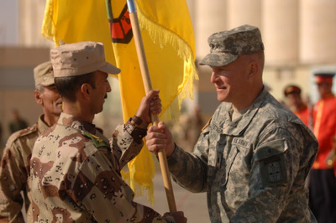 U.S. Army Lt. Col. Scott Wuestner (right) of Command Task Force Thunder passes the colors to Iraqi Lt. Col. Salahaddin Abdul Somad Hogar of the 3rd Battalion, 3rd Brigade, 2nd Iraqi Army Division, during a change of responsibility ceremony in Makhmur, Iraq, on Dec. 27, 2005. Wuestner is the commander of the 4-11th Field Artillery. 