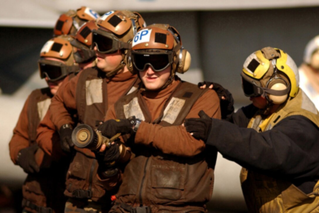 Airman Lisa Cummings (right) instructs a hose team how to correctly extinguish a simulated aircraft fire during a flight deck general quarters drill aboard the aircraft carrier USS Harry S. Truman (CVN 75) on Feb. 8, 2005. The Truman Carrier Strike Group is on deployment in the Persian Gulf. Cummings is a Navy aviation boatswain's mate. 