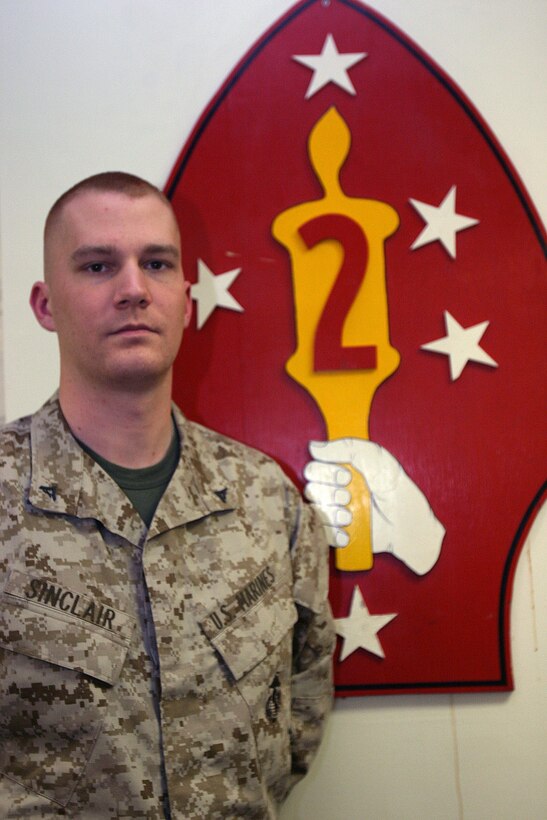 MARINE CORPS BASE CAMP LEJEUNE, N.C. - Lance Cpl. Joshua A. Sinclair, a Lansing, Mich. native and Marine Air Ground Task Force planner for 2d Marine Division stands by the 2d Marine Division sign in his office. Sinclair, spends many hours in his office making sure the division has the correct people and equipment to deploy.