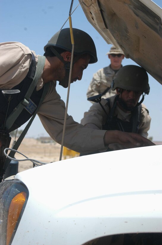 CAMP ALI Ar Ramadi, Iraq - Two members of the Iraqi Security Forces search under the hood of a vehicle while Lance Cpl. Nick C. Strowmatt, a grenadier and instructor with the Combined Action Platoon, Company B, 1st Battalion, 5th Marine Regiment, stands back and supervises during a training session here. The 22-year-old from Kailua, Hawaii, and his fellow Marines with the platoon are responsible for training new members of the Iraqi Security Forces during the infantry battalion's deployment in support of Operation Iraqi Freedom.   Photo by: Cpl. Tom Sloan