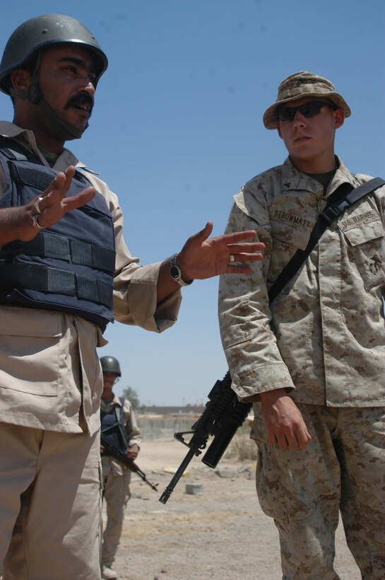 CAMP ALI Ar Ramadi, Iraq (May 31, 2005) - An Iraqi Police Officer instructs his officers during a training mission here while Lance Cpl. Nick C. Strowmatt, a grenadier and instructor with the Combined Action Platoon, Company B, 1st Battalion, 5th Marine Regiment, stands by and supervises. The 22-year-old from Kailua, Hawaii, and his fellow Marines with the platoon are responsible for training new members of the Iraqi Security Forces - police and New Iraqi Army Soldiers - during the infantry battalion's deployment in support of Operation Iraqi Freedom. The platoon has trained 300 soldiers and 300 police officers since assuming the training role two months ago. Photo by: Cpl. Tom Sloan