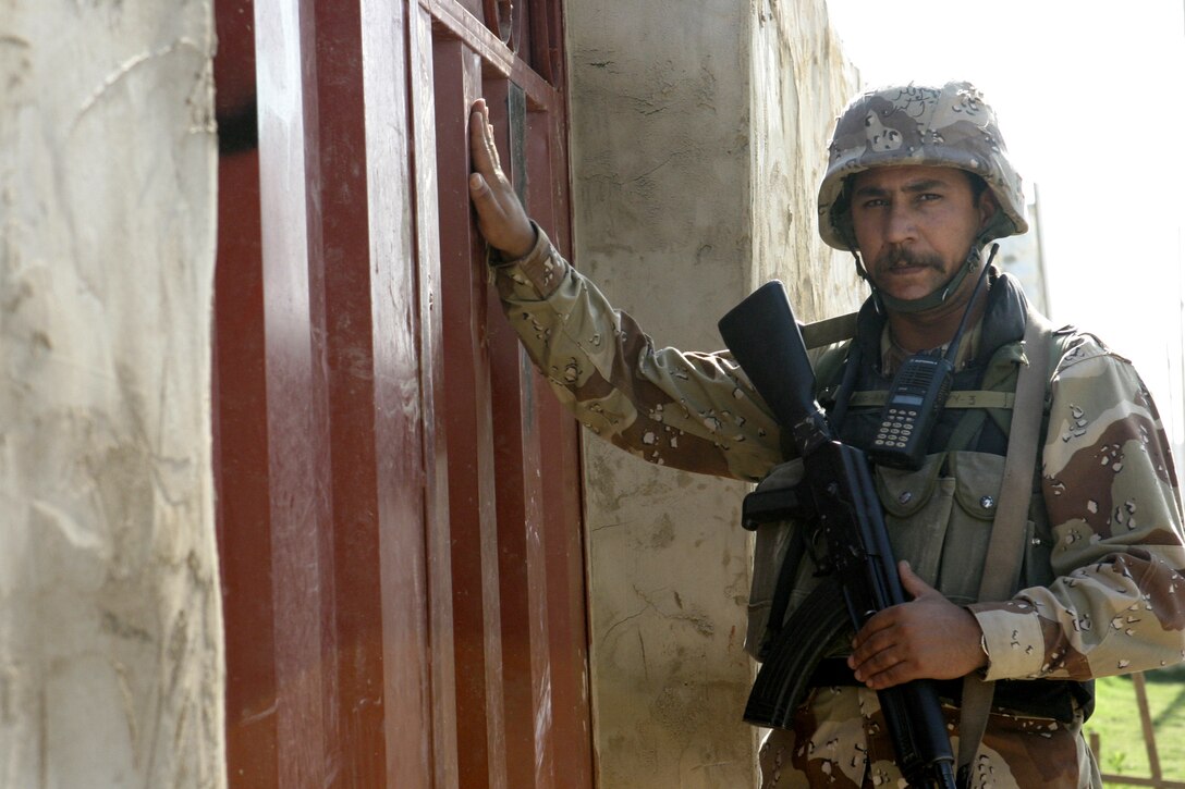 FALLUJAH, Iraq - An Iraqi soldier knocks on a gate door outside a residence here June 1 during 'Operation Hard Knock,' as his fellow troops prepare to search it for weapons.  The soldiers worked alongside Marines from Company B, 1st Battalion, 6th Marine Regiment to search through every house and field in a sector of Fallujah, confiscate numerous weapons and explosive materials, and detain four known insurgent supporters.
