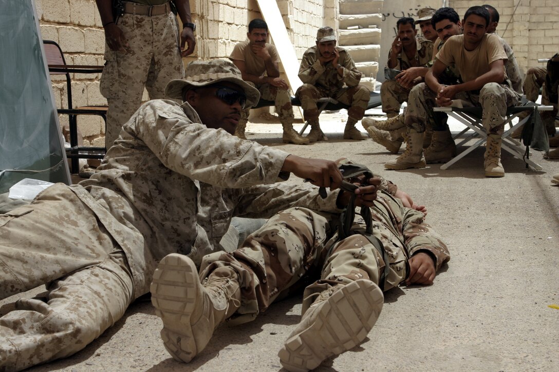 FALLUJAH, Iraq - Petty Officer 2nd Class Phillip Jean-Gilles, a corpsman working with 1st Battalion, 6th Marine Regiment's Iraqi Security Forces training cadre, demonstrates how to tie a tourniquet before a class of Iraqi soldiers and policemen here Aug. 1.  Since mid-March, battalion personnel have trained approximately 600 Iraqi personnel on topics such as first aid in combat, infantry tactics, and convoy driving skills.  Iraqi forces are fully integrated into every operation the battalion's Marines and sailors conduct in and around the city.