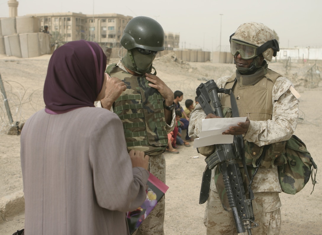 FALLUJAH, Iraq - Sgt. Kent D. Padmore, guard chief for Fallujah's Civil-Military Operations Center's Entry Control Point-7, and an interpreter speak with a local woman during a toy giveaway outside the center Aug. 11.  U.S. Marines and Iraqi police distribute clothes and toys to local children outside the center every week, while local and military officials inside issue compensation payments and brainstorm ideas to rebuild the city's infrastructure.