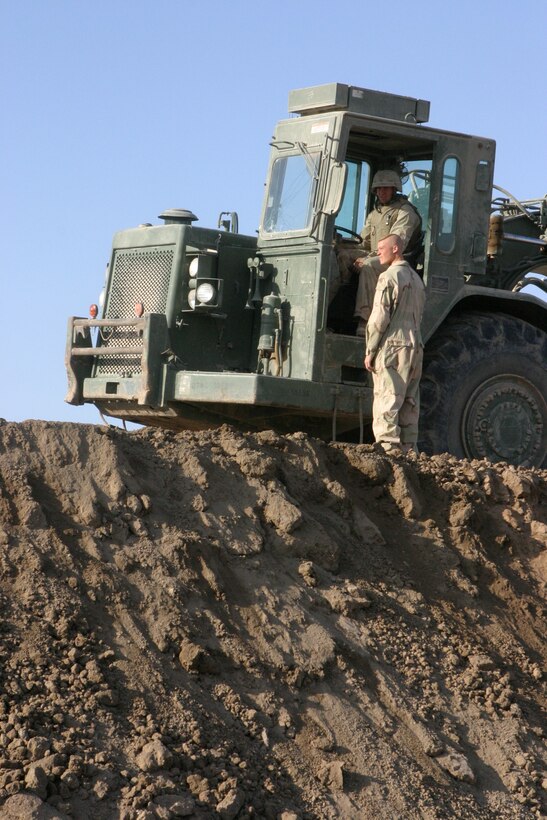 CAMP HABBANIYAH, Iraq - A scrapers operator with Heavy Equipment Platoon, 8th Engineer Support Battalion, talks with another Marine as he waits to move forward along the berm to add a layer of dirt. They must bring each berm to a minimum of 15 feet in height.