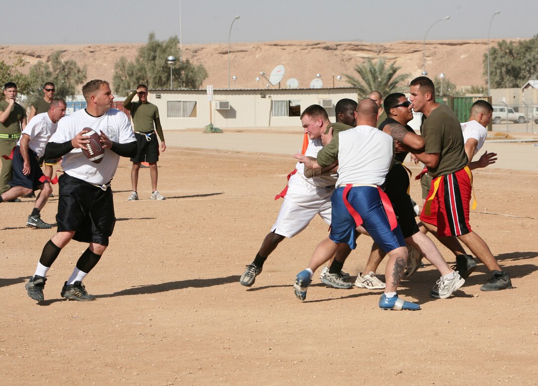 Staff Sgt. Bruce Martin (holding football), quarterback for the “Gunrunners,” looks for an open teammate while his offensive line attempts to block their opponents during a flag football tournament aboard Al Asad Air Base, Iraq, Dec. 13, 2009. Each month, service members and civilians gather at the stadium aboard the base to compete for the gold medal.