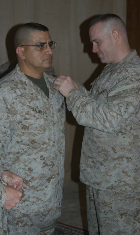 CAMP HURRICANE POINT Ar Ramadi, Iraq (May 1, 2005) - Maj. Phillip J. Treglia, the operations officer for Headquarters and Service Company, 1st Battalion, 5th Marine Regiment, pins master gunnery sergeant chevrons on Roland Salinas during his promotion ceremony here. The 42-year-old operations chief with H&S Company and San Antonio, Texas, native reached the final rung on the Marine Corps' ladder of success for enlisted personnel after serving more than 24 years. Salinas reenlisted in Iraq and has three years left on his twilight contract. Photo by Cpl. Tom Sloan