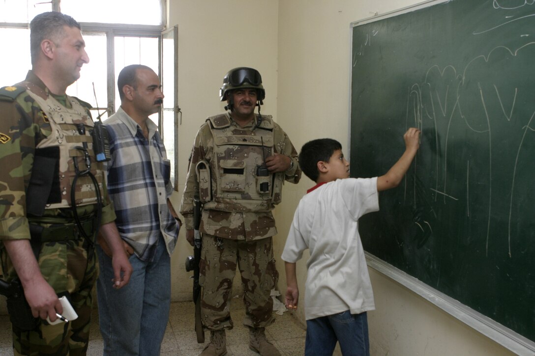 FALLUJAH, Iraq - From left to right: Iraqi Maj. Laith Jabbar Al Tememey, company commander for 1st Company, 1st Battalion, 2nd Brigade, Iraqi Security Forces, a school teacher, and a soldier, look on as a schoolchild doodles on a new chalkboard Iraqi soldiers donated to his school here May 2.  Iraqi Security Forces and Marine forces here visited local schools to distribute blackboards, school desks, and writing supplies as part of the ongoing joint civil-military mission, "Operation Blackboard."