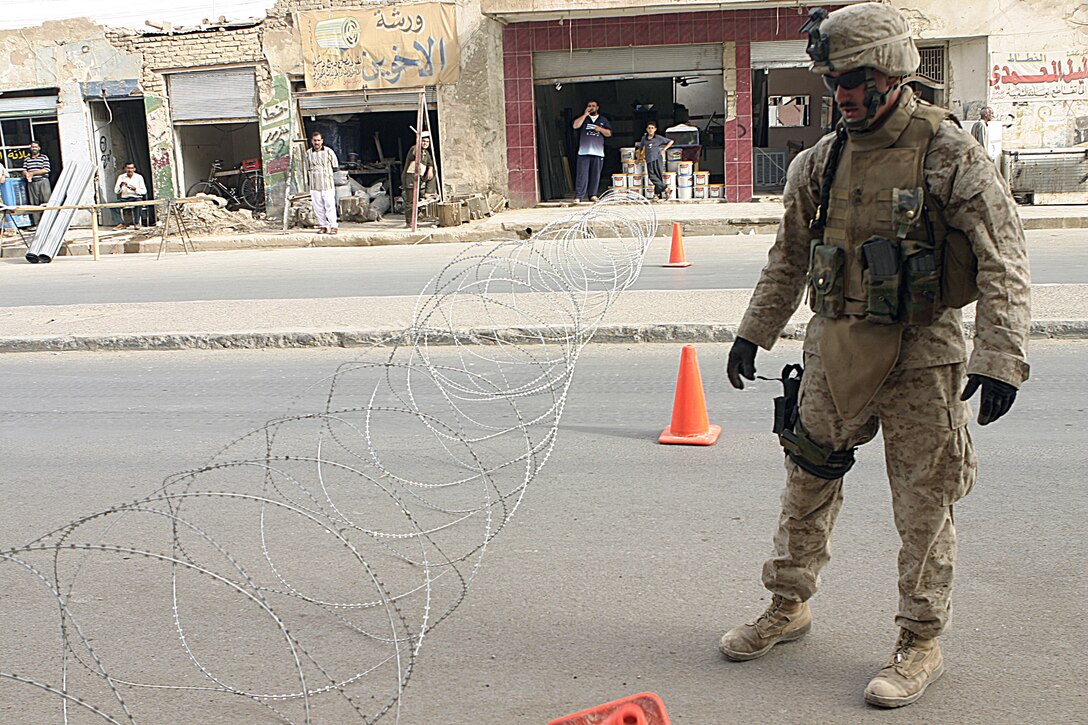 FALLUJAH, Iraq - Cpl. Ryan Casavant, an infantryman with Company W, 1st Battalion, 6th Marine Regiment, observes a concertina wire obstacle used to block a street here July 2.  Company W worked alongside 1st Battalion, 6th Marine Regiment infantrymen, Iraqi Security Forces and mechanized supporting elements to conduct Operation Rolling Barrage, during which the troops blocked off sections of Fallujah while roving infantrymen patrolled through the streets to disrupt insurgent activity.