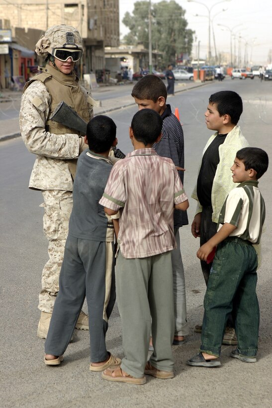 Lance Cpl. Daniel Ramos, an infantryman with Surveillance, Target and Acquisition (STA) platoon, Company W, 1st Battalion, 6th Marine Regiment, speaks with local children while providing security along a street corner here July 2.  The 19-year-old Orange Park, Fla. native worked alongside other Company W personnel, Iraqi Security Forces, and mechanized elements to conduct Operation Rolling Barrage, during which the troops blocked off sections of Fallujah while roving infantrymen patrolled through the streets to disrupt insurgent activity.