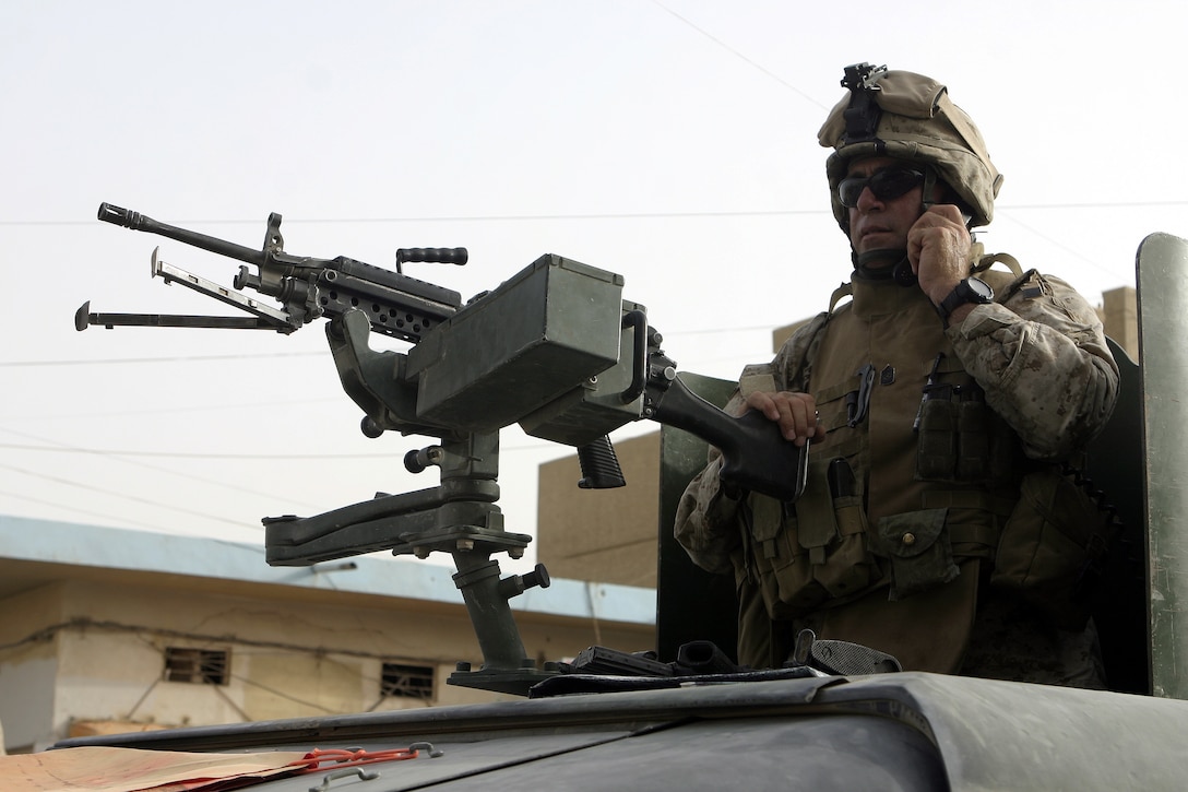 FALLUJAH, Iraq - Master Sgt. Luis Hernandez, Company W, 1st Battalion, 6th Marine Regiment's operations chief, mans his M249 Squad Automatic Weapon atop his vehicle here July 2 while providing security down a street.  Company W worked alongside 1st Battalion, 6th Marine Regiment infantrymen, Iraqi Security Forces and mechanized supporting elements to conduct Operation Rolling Barrage, during which the troops blocked off sections of Fallujah while roving infantrymen patrolled through the streets to disrupt insurgent activity.