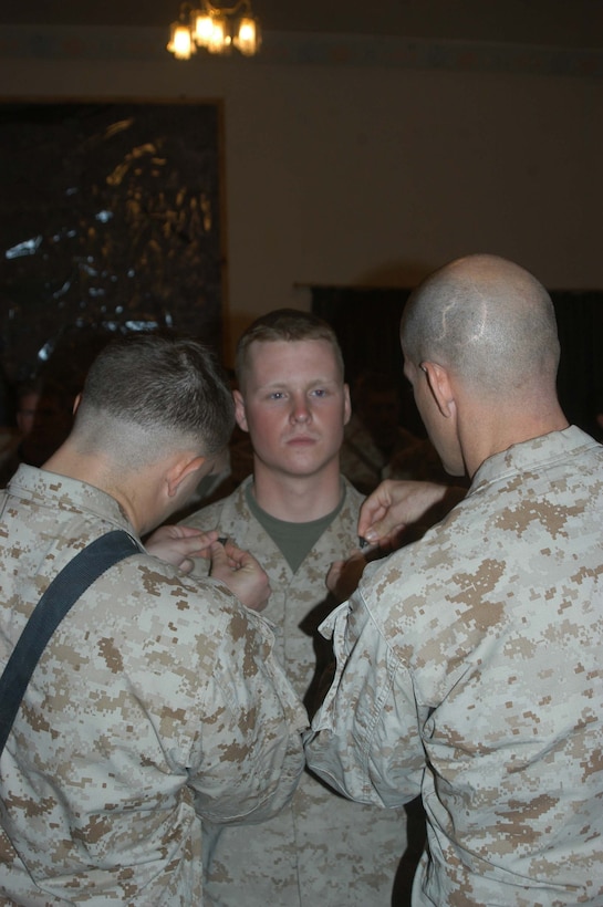 CAMP HURRICANE POINT Ar Ramadi, Iraq (Aug. 3, 2005) -Corporal Michael T. Wheat,(left) a mortar man with 4th Platoon, Company W, 1st Battalion, 5th Marine Regiment, and Capt. Michael J. Butler, Company W's commander, pin corporal chevrons on the collar of Joseph P. Nagel's blouse during a ceremony here Aug. 2. Nagel, a 22-year-old machine gunner with 4th Platoon and Dousman, Wis., native, was combat meritoriously promoted to the rank of corporal and received two Purple Hearts during the ceremony. Nagel was wounded June 15 and July 1 while conducting security and stability operations with his fellow Marines in support of Operation Iraqi Freedom. An enemy bullet hit Nagel in the left forearm and shrapnel from an improvised explosive caught him in the left hand. He was riding in the turret of a humvee manning a MK-19 Grenade Launcher during both close calls, which resulted in minor injuries.  Nagel is two-time veteran of the fighting in Iraq. He was with 1st Battalion, 5th Marines last year for OIF II, fought in Fallujah and made it out unscathed. Photo by: Cpl. Tom Sloan