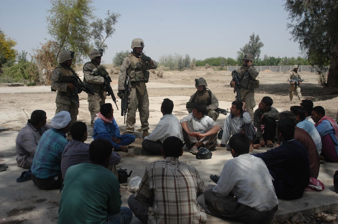 AR RAMADI, Iraq (April 2, 2005) -Corporal Jeff B. Starr, a section leader with 1st Squad, 4th Platoon, Company B, 1st Battalion, 5th Marines, and his fellow devil dogs encountered a group of Iraqi men sitting down having lunch at the site where they were conducting a weapons caches search. The 21-year-old from Seattle questioned the men and determined them to be of no threat. Marines with 4th Platoon, Company B, 1st Battalion, 5th Marine Regiment and leathernecks of Company A, 1st Combat Engineer Battalion teamed up and discovered four 120 mm shells, a 155 mm shell; several live and empty 7.62 rounds, explosive detonation cord, a live fragmenting grenade and one rocket launcher during the five-hour search conducted on several acres of farmland along the banks of the Euphrates River on the edge of the city here. Photo by Cpl. Tom Sloan