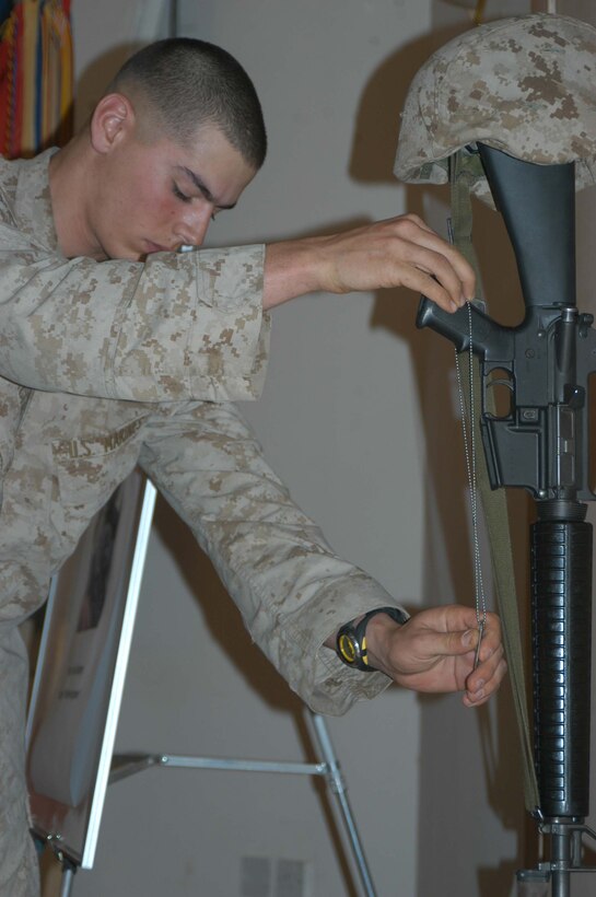 CAMP HURRICANE POINT, Ar Ramadi, Iraq (April 25, 2005) - Lance Cpl. Chris G. Garcia, a rifleman with 1st Platoon, Company A, 1st Battalion, 5th Marine Regiment, hangs the dog tags one of his fellow comrades once wore on the handle of an M-16. Marines with 1st Battalion, 5th Marine Regiment, held a dual memorial ceremony here in honor of Lance Cpl. Marty G. Mortenson, 22, of Flagstaff, Ariz., and Cpl. Kelly M. Cannan, 21, of Lowville, N.Y. Both warriors were killed by the same improvised explosive device attack while traveling in a convoy April 20. They were on their third deployment supporting Operation Iraqi Freedom. Photo by Cpl. Tom Sloan
