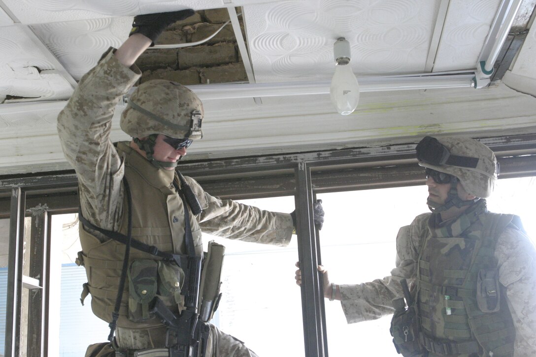 FALLUJAH, Iraq - A Marine with Company B, 1st Battalion, 6th Marine Regiment, left, and Coco, a translator with Company B, right, look for possible weapons and enemy intelligence materials hidden atop ceiling tiles inside a building here May 3.  Company B personnel worked alongside Iraqi Security Forces to apprehend an insurgent supporter known for laying improvised explosive devices here and recruiting others to do the same.