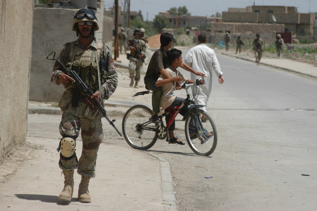 AR RAMADI Iraq (June 3, 2005) - An Iraqi Security Force member walks past an Iraq man and two boys riding a bicycle during a mission in the city. Seven members of the ISF accompanied Marines with 1st Squad, 2nd Platoon, Company C, 1st Battalion, 5th Marine Regiment, and, together, conducted a mission to listen to messages a mosque was broadcasting over its loudspeakers during midday prayer. Marines with Company C are having a positive influence on the locals in their area of operations by working with the ISF. Photo by: Cpl. Tom Sloan