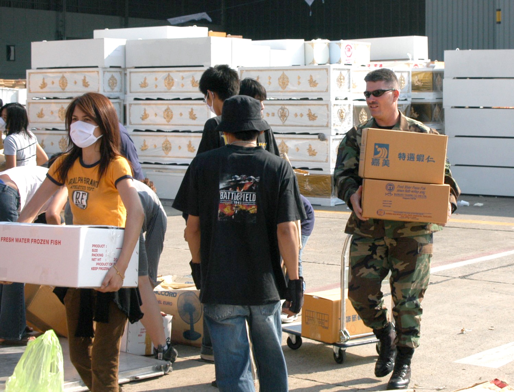 BANGKOK, Thailand -- An Airman here carries boxes of relief supplies Jan. 1 at the international airport.  He and 100 others from the 353rd Special Operations Group are flying supplies to the tsunami-hit areas of southern Thailand.  In the background are hundreds of caskets.  The 353rd SOG Airmen are assigned to Kadena Air Base, Japan.  (U.S. Air Force photo by Master Sgt. Michael Farris)