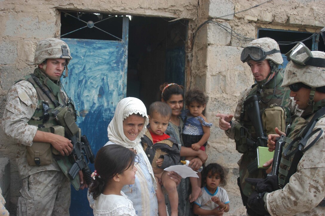 AR RAMADI, Iraq (May 4, 2005) -Corporal Michael L. Godfrey(left), assistant noncommissioned officer with 5th Civil Affairs Group, 1st Battalion, 5th Marine Regiment, provides security at a house here while Maj. Benjamin B. Busch(center), 5th CAG's team leader and Ricky Wissam, a translator, speak to the mother of an Iraqi boy who has a server urinary tract infection. Godfrey, 21, of Mount Zion, Md., was conducting a routine CAG patrol through a neighborhood less than a week ago when he discovered the ailing child. Marines with 5th CAG coordinated for the boy to be taken to a local hospital to receive medical aid for his illness. If left untreated, the infection could've entered his kidneys and caused them to fail. Photo by Cpl. Tom Sloan
