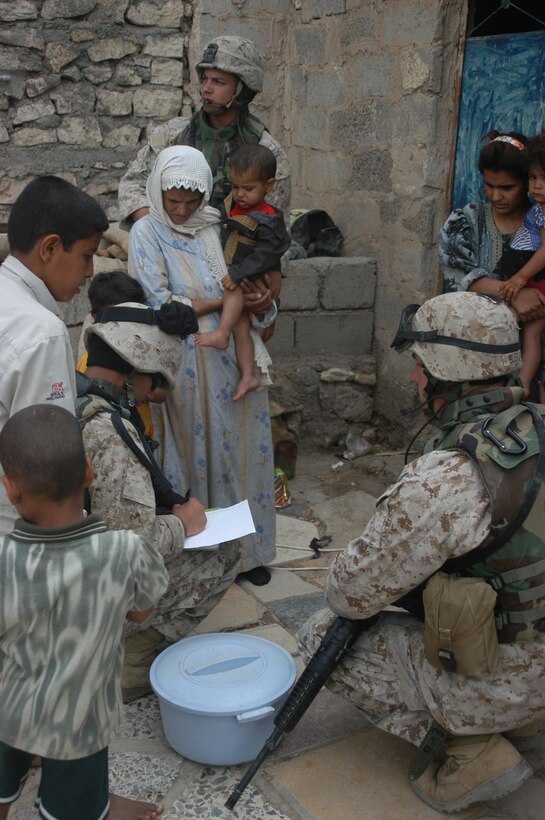 AR RAMADI, Iraq (May 4, 2005) -Corporal Michael L. Godfrey(center back), assistant noncommissioned officer with 5th Civil Affairs Group, 1st Battalion, 5th Marine Regiment, provides security at a house here while Ricky Wissam, a translator, writes on piece of paper the name of a doctor Maj. Benjamin B. Busch, 5th CAG's team leader, wants the mother find at the hospital to treat her sick son. The Iraqi boy has a server urinary tract infection. If left untreated, the infection could've entered his kidneys and caused them to fail. Godfrey, 21, of Mount Zion, Md., was conducting a routine CAG patrol through a neighborhood less than a week ago when he discovered the ailing child. Marines with 5th CAG coordinated for the boy to be taken to a local hospital to receive medical aid for his illness. Photo by Cpl. Tom Sloan
