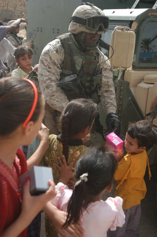 AR RAMADI, Iraq (May 4, 2005) - Gunnery Sgt. Wayne B. McClam, team chief with 5th Civil Affairs Group, 1st Battalion, 5th Marine Regiment, hands out dolls to Iraqi children on a city street here. The 37-year-old from Lake City, S.C., and other Marines with 5th CAG presented the children with gifts of soccer balls, clothes, dolls and wristwatches. The effort was a diversion tactic designed to keep the insurgency from learning the real reason for their visit. Marines with 5th CAG coordinated for an Iraqi boy with a server urinary tract infection to receive treatment at a local hospital. Photo by Cpl. Tom Sloan