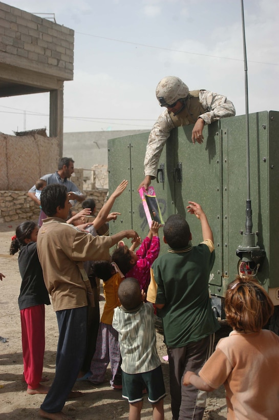 AR RAMADI, Iraq (May 4, 2005) -From the back of a high-back Humvee, Sgt Hector Martinez Jr., noncommissioned officer with 5th Civil Affairs Group, 1st Battalion, 5th Marine Regiment, hands out dolls to Iraqi children on a city street here. The 28-year-old from Fontana, Mont., and other Marines with 5th CAG presented the children with gifts of soccer balls, clothes, dolls and wristwatches. The effort was a diversion tactic designed to keep the insurgency from learning the real reason for their visit. Marines with 5th CAG coordinated for an Iraqi boy with a server urinary tract infection to receive treatment at a local hospital. Photo by Cpl. Tom Sloan