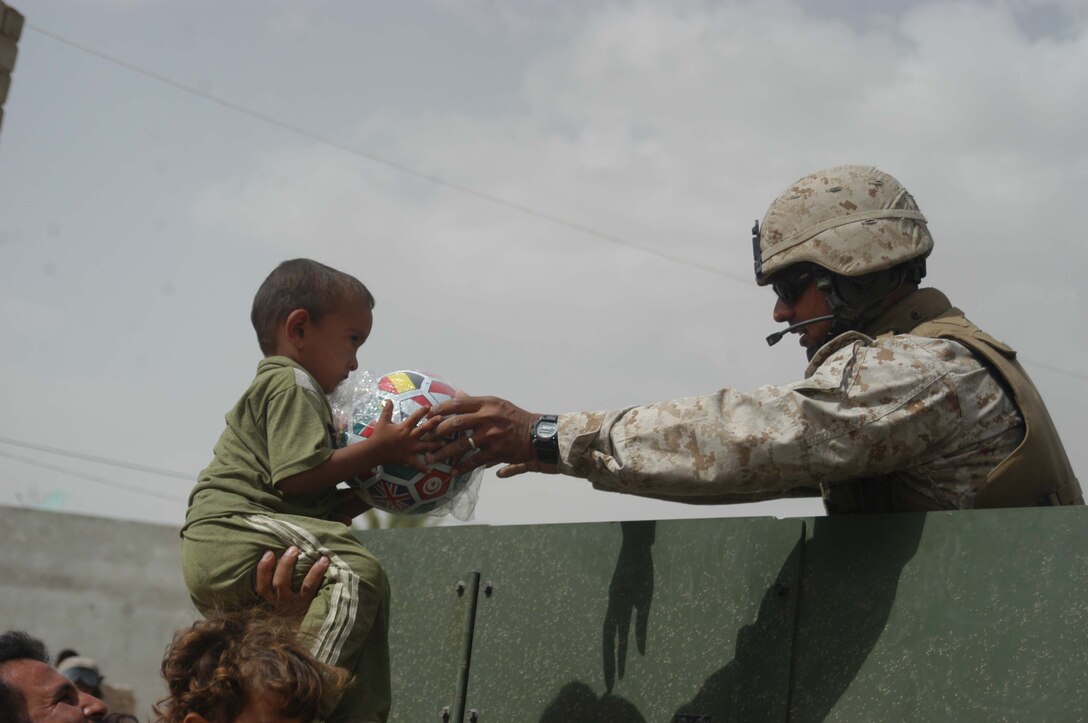 AR RAMADI, Iraq (May 4, 2005) -From the back of a high-back Humvee, Sgt Hector Martinez Jr., noncommissioned officer with 5th Civil Affairs Group, 1st Battalion, 5th Marine Regiment, hands an Iraqi boy a soccer ball on a city street here. The 28-year-old from Fontana, Mont., and other Marines with 5th CAG presented the children with gifts of soccer balls, clothes, dolls and wristwatches. The effort was a diversion tactic designed to keep the insurgency from learning the real reason for their visit. Marines with 5th CAG coordinated for an Iraqi boy with a server urinary tract infection to receive treatment at a local hospital. Photo by Cpl. Tom Sloan