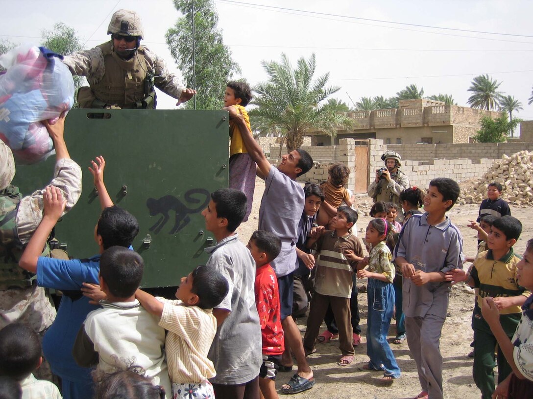 AR RAMADI, Iraq (May 4, 2005) - From the back of a high-back Humvee, Sgt Hector Martinez Jr., noncommissioned officer with 5th Civil Affairs Group, 1st Battalion, 5th Marine Regiment, lowers a bag of soccer balls into the arms of Cpl. Michael L. Godfrey, assistant noncommissioned officer with 5th CAG, who's standing in a street here. The 28-year-old from Fontana, Ca., and other Marines with 5th CAG presented the children with gifts of soccer balls, clothes, dolls and wristwatches. The effort was a diversion tactic designed to keep local residents from intruding and to protect the privacy of a family there. Marines with 5th CAG coordinated for an Iraqi boy with a severe urinary tract infection to receive treatment at a local hospital. Contributed photo