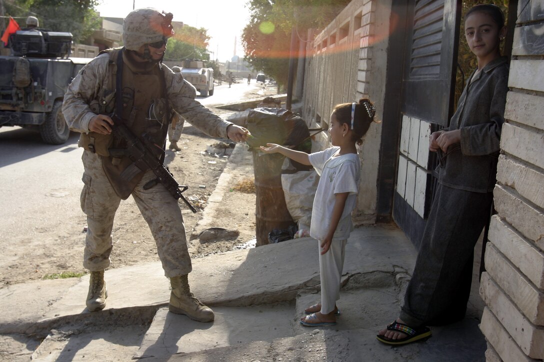 FALLUJAH, Iraq - Corporal Justin Henshaw, an infantryman with 4th Combined Anti-Armor Team, Weapons Company, 1st Battalion, 6th Marine Regiment, hands candy to local children during a recent patrol here.  The 25-year-old St. Simons Island, Ga. native traded a promising career in acting and personal training to fight the Global War on Terror overseas, where he claims to enjoy helping the Iraqi people rebuild their nation.