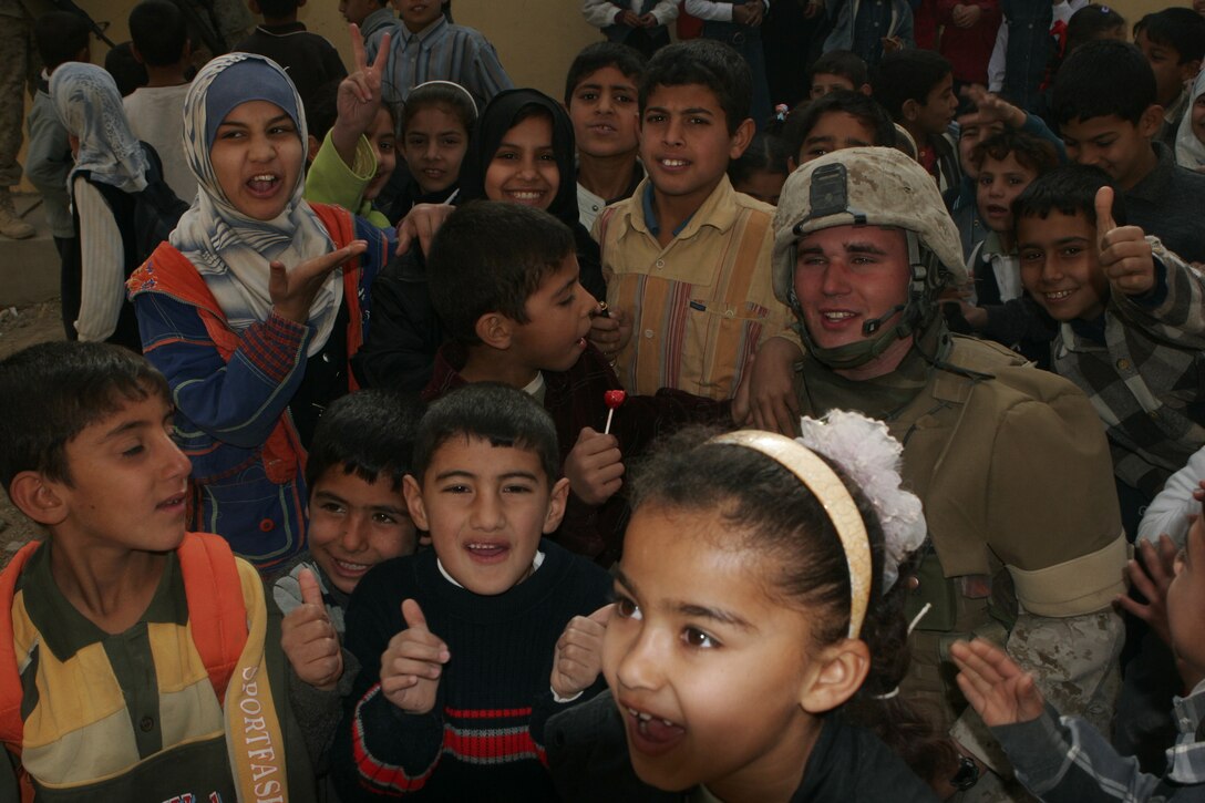Twenty-two-year-old Lance Cpl. Robert Hancock, saw gunner, Team 4, Detachment 4, 6th Civil Affairs Group, 2nd Marine Division, is crowded by Iraqi children in Saqlawiyah, Iraq.  The Fort Mill, S.C., native, helped distribute school supplies and toys to the school children.