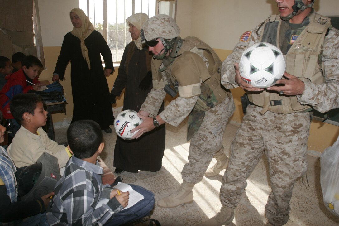 Twenty-two-year-old Lance Cpl. Robert Hancock, saw gunner, Team 4, Detachment 4, 6th Civil Affairs Group, 2nd Marine Division, hands a soccer ball to an Iraqi child during a recent visit to Saqlawiyah, Iraq. The soccer balls were donated by the 7th and 8th grade students from Kailua Intermediate School, in Kailua, Hawaii.