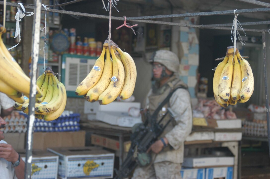 AR RAMADI, Iraq (May 27, 2005) - Bananas hang from strings at the city's marketplace as Lance Cpl. Timothy R. Curridier a squad automatic machine gunner with 3rd Squad, 4th Platoon, Company A, 1st Battalion, 5th Marine Regiment, walks past during a patrol. The 21-year-old from Milwaukee his fellow 4th Platoon warriors conducted a four-hour aggressive-foot-patrol through several neighborhoods and the city's marketplace. The Marines searched 12 houses and talked to numerous locals during the mission, which was conducted in an attempt to stifle insurgent activity and inform citizens why Marines and coalition forces are occupying Ramadi. The Marines handed out pro-coalition forces and pro-Iraqi government fliers, which had a number to call coalition forces to report insurgent activity. Photo by: Cpl. Tom Sloan