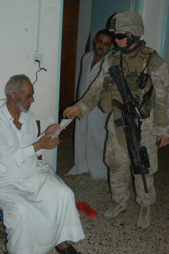 AR RAMADI, Iraq (May 29, 2005) - Corporal Vernon E. Corbett, a rifleman and squad leader for 3rd Squad, 4th Platoon, Company A, 1st Battalion, 5th Marine Regiment, hands an Iraqi man a pro-coalition forces flier during a mission in the city here. The flier has a telephone number civilians can call and report insurgent activity. The 2000 Hickman Mills High School graduate and his fellow squad members searched several houses for weapons caches and questioned residents if they knew of insurgent activity.  Photo by: Cpl. Tom Sloan