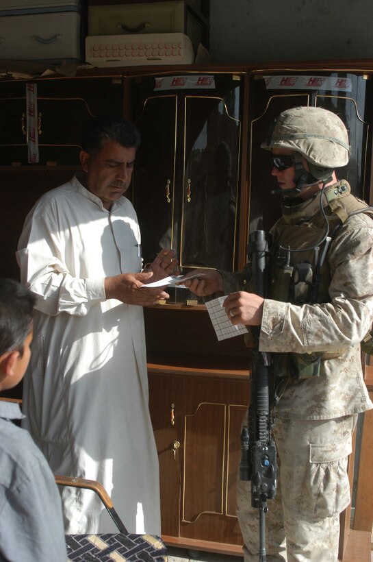 AR RAMADI, Iraq (May 29, 2005) - Corporal Vernon E. Corbett, a rifleman and squad leader for 3rd Squad, 4th Platoon, Company A, 1st Battalion, 5th Marine Regiment, hands an Iraqi man a pro-coalition forces flier during a mission in the city here. The flier has a telephone number civilians can call and report insurgent activity. The 2000 Hickman Mills High School graduate and his fellow squad members searched several houses for weapons caches and questioned residents if they knew of insurgent activity.  Photo by: Cpl. Tom Sloan