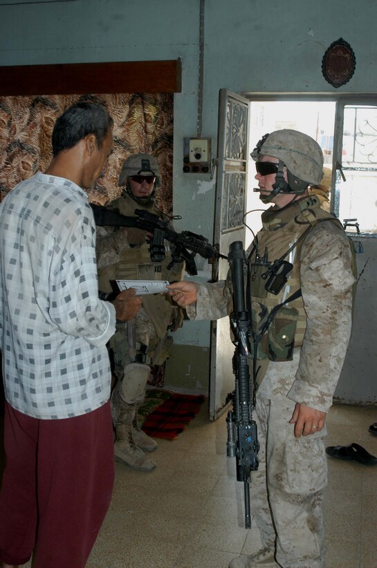 AR RAMADI, Iraq (May 29, 2005) - Corporal Vernon E. Corbett, a rifleman and squad leader for 3rd Squad, 4th Platoon, Company A, 1st Battalion, 5th Marine Regiment, hands an Iraqi man a pro-coalition forces flier during a mission in the city here. The flier has a telephone number civilians can call and report insurgent activity. The 2000 Hickman Mills High School graduate and his fellow squad members searched several houses for weapons caches and questioned residents if they knew of insurgent activity.  Photo by: Cpl. Tom Sloan