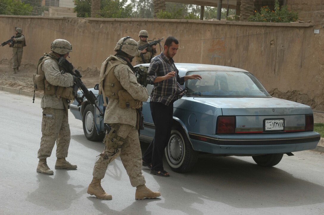 AR RAMADI Iraq (July 5, 2005) -Marines with 2nd Platoon, Company W, 1st Battalion, 5th Marine Regiment, stop a man driving in the street and search his car during a mission in the city here July 5. The Marines conducted a proactive operation to encourage Ar Ramadi citizens to move their trashcans off the streets and place them in the yards and behind their homes. The Iraqi government recently distributed new, orange, industrial-sized trash containers throughout the city for citizens to use to clean up rubbish, but Marine officials with the 1st Battalion, 5th Marines suspect insurgents will exploit them for terror and place improvised explosive devices in them. Photo by Cpl. Tom Sloan