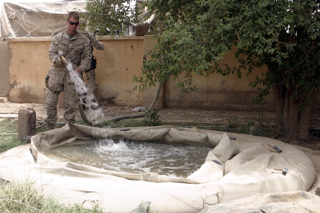 SAQLAWIYAH, Iraq - Cpl. Joseph Plank, a motor transport operator with 1st Battalion, 6th Marine Regiment, refills an infantry base's water supply here July 18.  Plank is one of many Marines who perform daily logistics runs to the infantrymen's operational headquarters to re-supply them with water, fuel, and food rations, along with replacing broken appliances and vehicles.