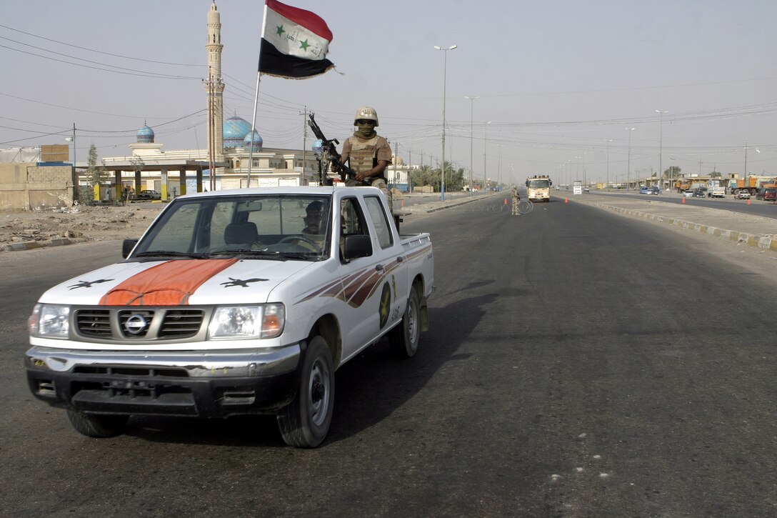 FALLUJAH, Iraq - Iraqi soldiers drive past a Marine vehicle check point set up along an intersection here July 19.  Iraqi Security Forces worked alongside 1st Battalion, 6th Marine Regiment personnel and mechanized supporting elements to block off sections of Fallujah, while roving infantrymen patrolled through the streets to disrupt insurgent activity.