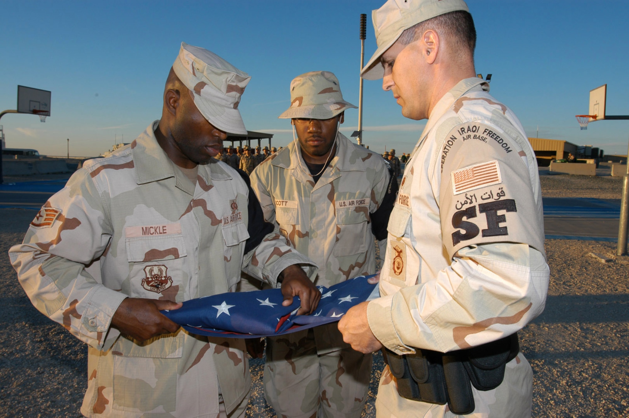 SOUTHWEST ASIA -- Staff Sgt. Denoris Mickle (left) and Senior Airman Cory Lenzmeir (right) fold the U.S. flag while Staff Sgt. Lydell Scott waits to receive the colors during a formal retreat ceremony at a forward-deployed location.  The Airmen are members of the 386th Air Expeditionary Wing Honor Guard.  The retreat ceremony is used to mark the end of the duty day and involves the lowering of both the U.S. and host nation flags.  (Digitally altered U.S. Air Force photo by Capt. Aaron Burgstein)