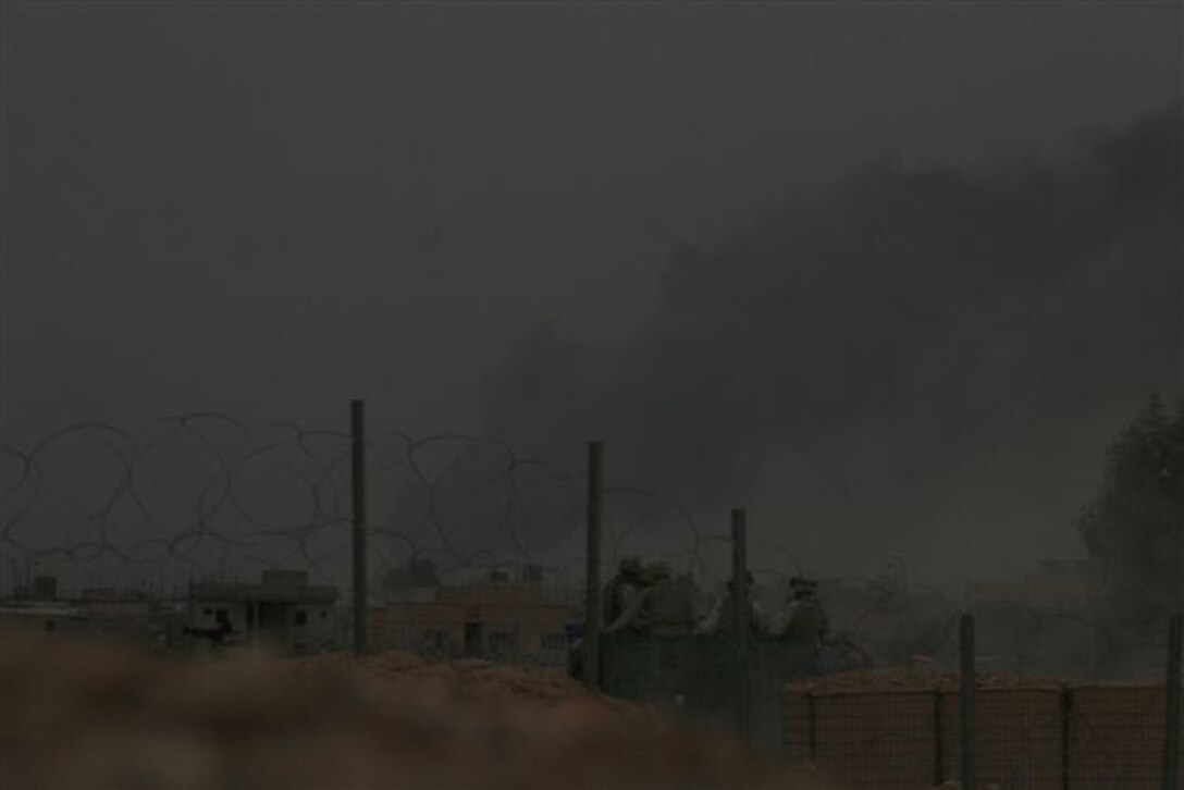 HUSAYBAH, Iraq ? Marines in the back of a humvee on the move in the foreground as smoke rises from Husaybah during fighting here, Nov. 6. The Marines, assigned to Headquarters and Service Company, 2nd Battalion, 1st Marine Regiment, and Iraqi soldiers with 1st Battalion, 1st Brigade, 1st Division, Iraqi Army, participated in the recent offensive against insurgents within border towns on the Lower Euphrates River Valley.